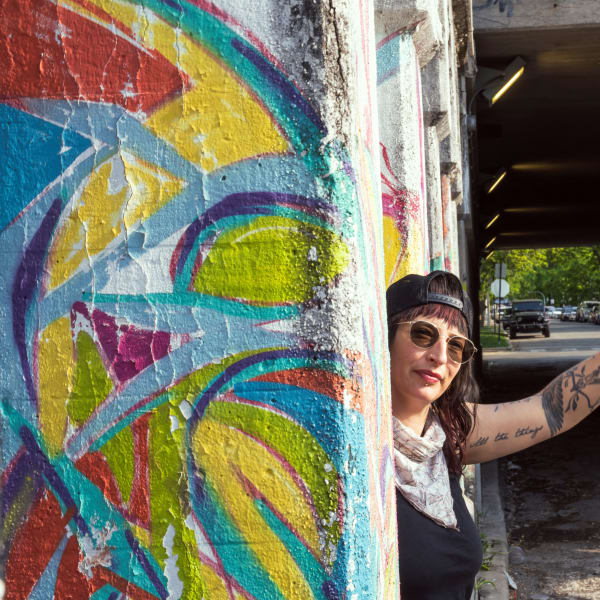 A woman holding a gay pride flag in front of a colorful mural.
