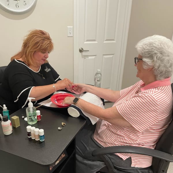 Two women face each other over a manicure table, as one woman gives the other woman a manicure.