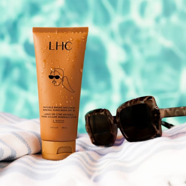 a bottle of LHC sunscreen on a towel next to a pair of sunglasses