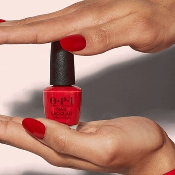 A pair of manicured hands holding a bottle of red nail polish