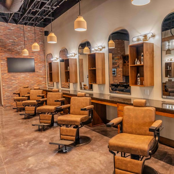 A row of brown barbershop chairs, stations and large arched mirrors at Parlor by Thompson and Company.