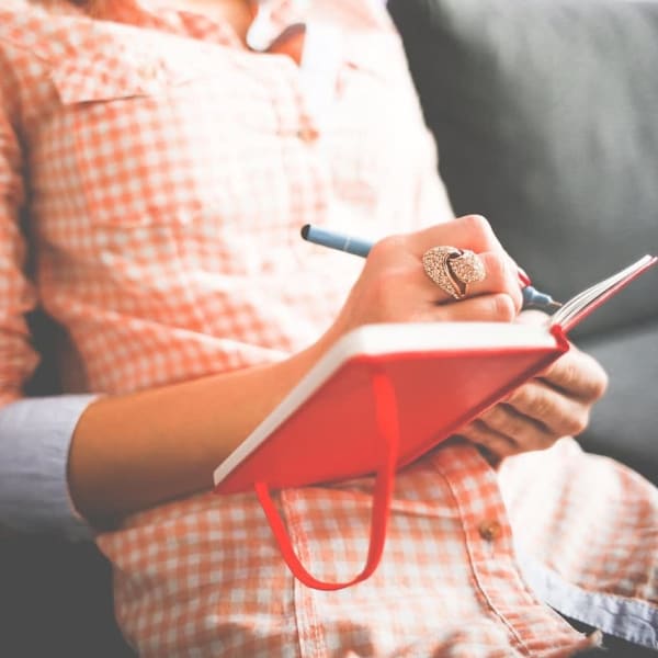 The torso of a woman, writing in a book.
