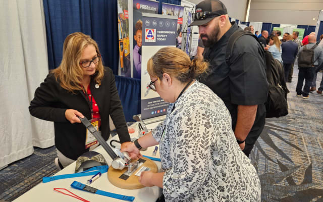 Attendees visit the AMF Bruns vendor booth in the expo hall, examining a wheelchair securement device while speaking with an exhibitor about safety equipment.