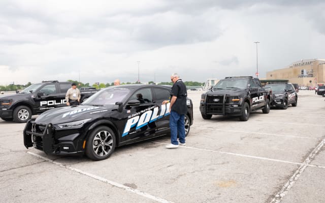 A lineup of police vehicles waiting to be test-driven is shown. They include a Ford Mustang Mach-E, a Ford F-150 Police Responder, and a Ford Police Interceptor Utility.