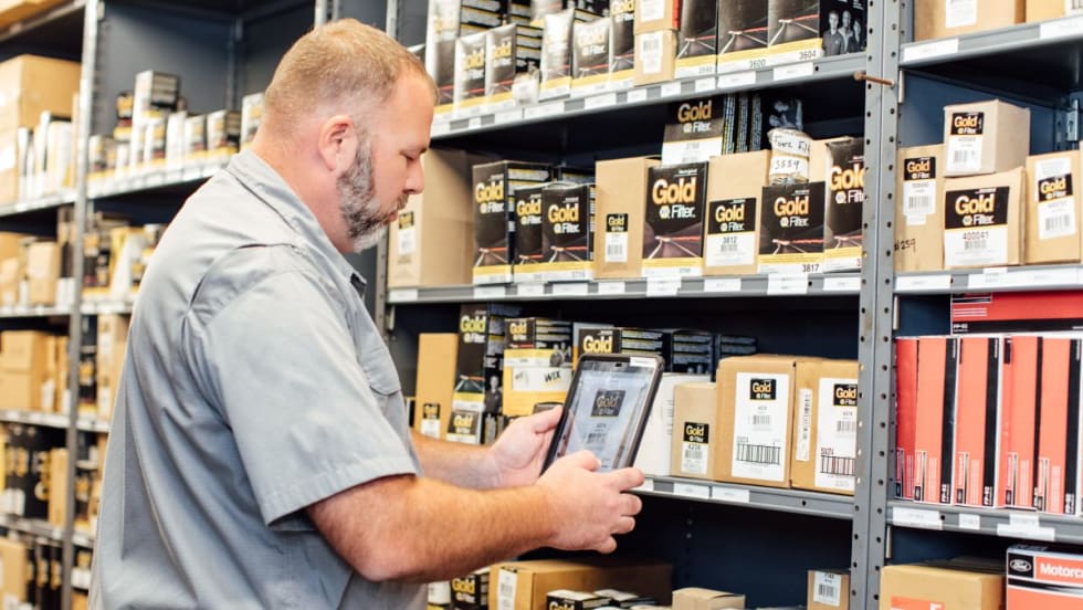 Man standing in front of parts shelf in workshop.