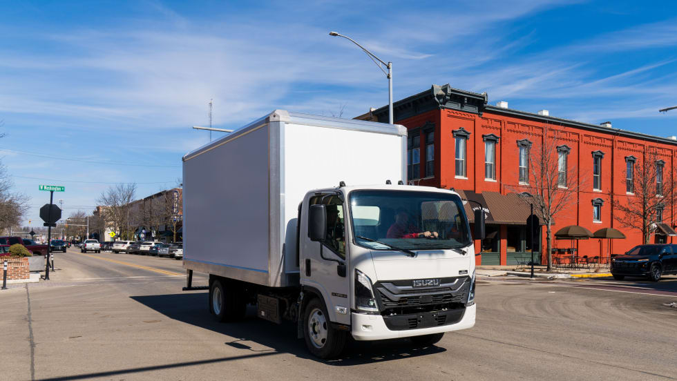 Isuzu commercial box truck driving in an urban area, representing a new body program with Aebi Schmidt that provides preconfigured, work-ready trucks for fleet customers.