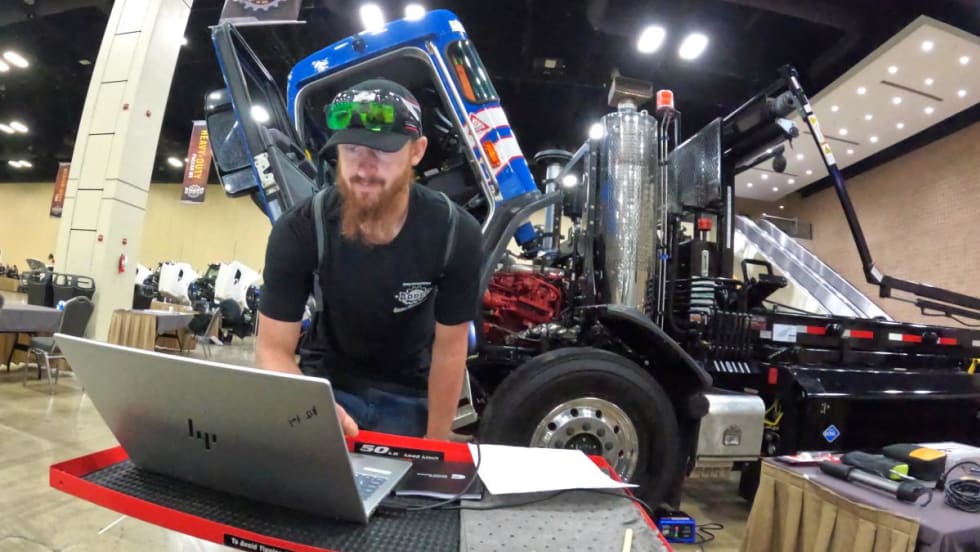 Male technician bent over a laptop computer in front of a line of CNG trucks in a maintenance shop.