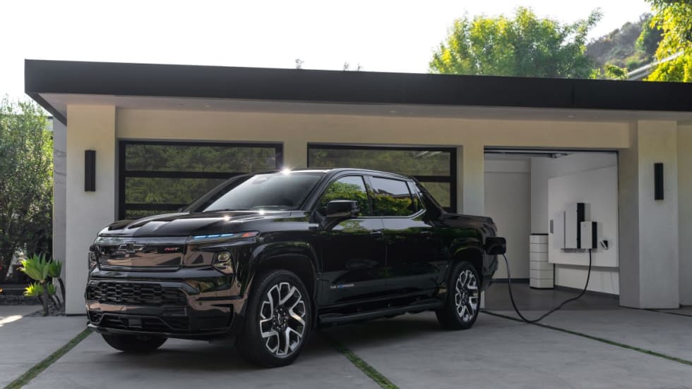 Pickup truck sits outside luxury home's garage getting charged.