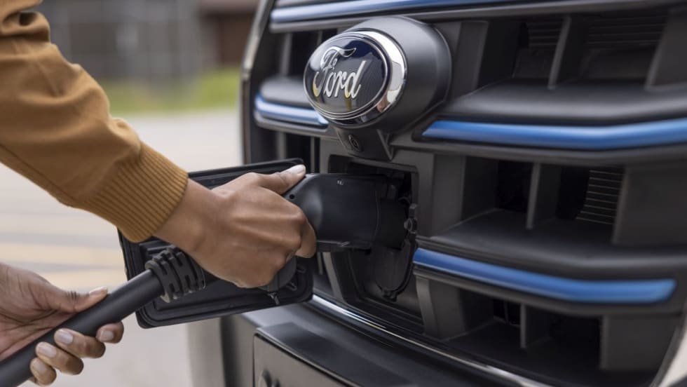 An electric charger plugged into the front grille and charging a Ford E-Transit 