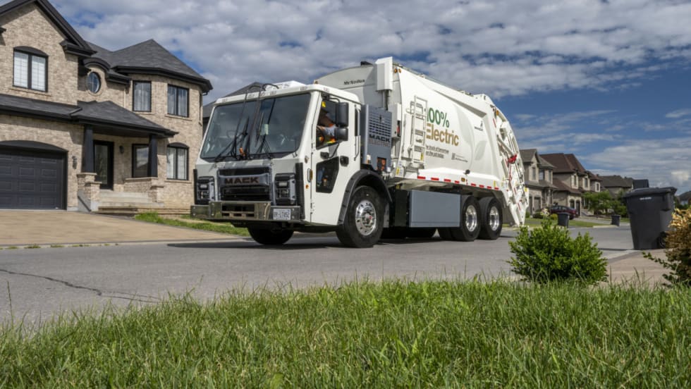A white refuse truck, or garbage truck, drives down the road.