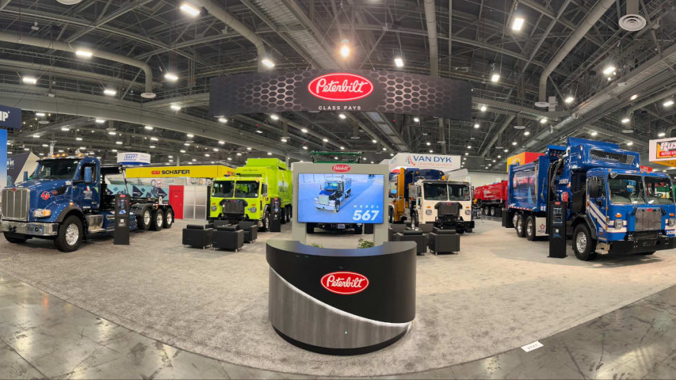 Four Peterbilt refuse trucks are parked in an exhibit space at WasteExpo.