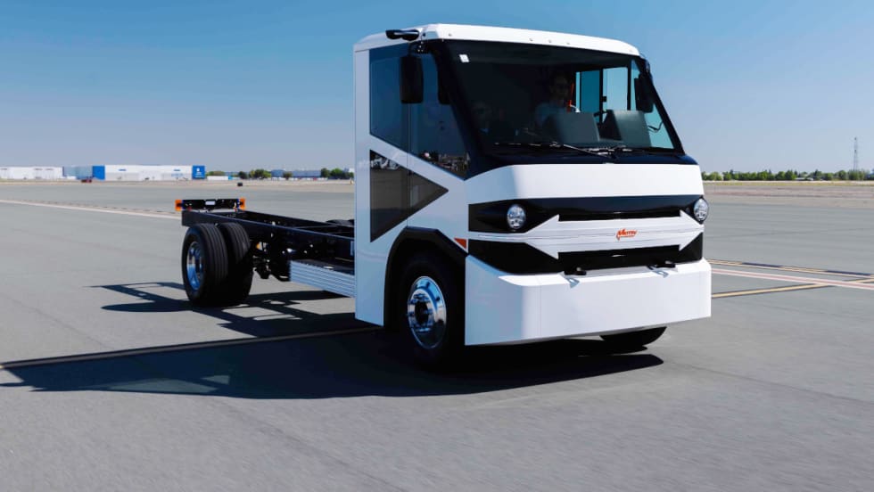 Front corner view of a white truck cap on a chassis parked at what looks like an airport.