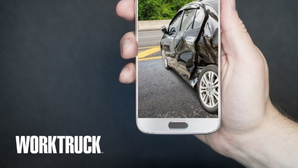 Person holding a cellphone with an image on the screen of a car that has been involved in a collision.