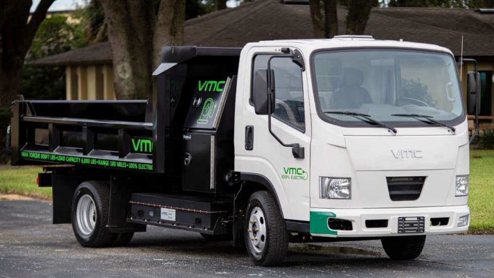 An electric truck with a white cab and a black bed is parked on a street.