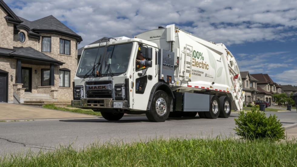 White refuse truck, garbage truck, drives down a residential street.