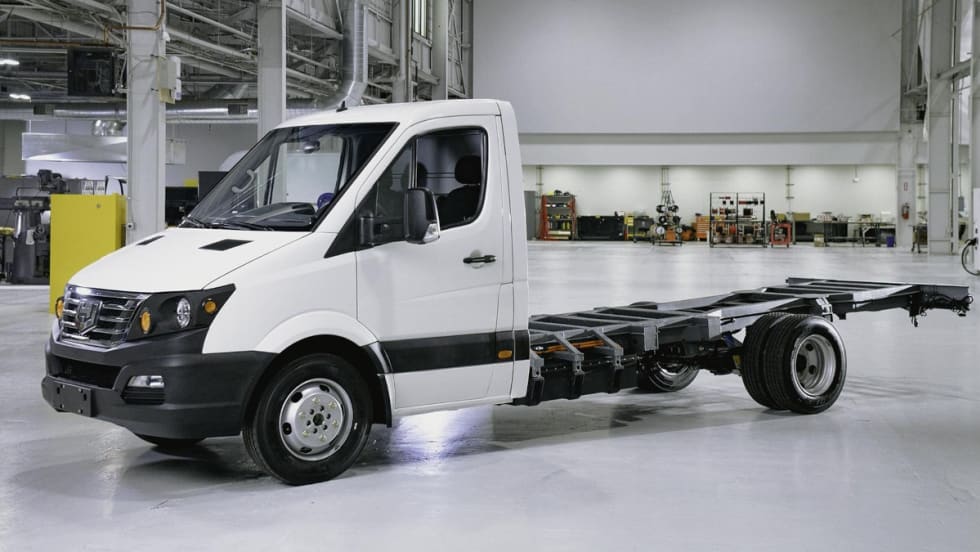White chassis cab truck is parked inside a building facing left.