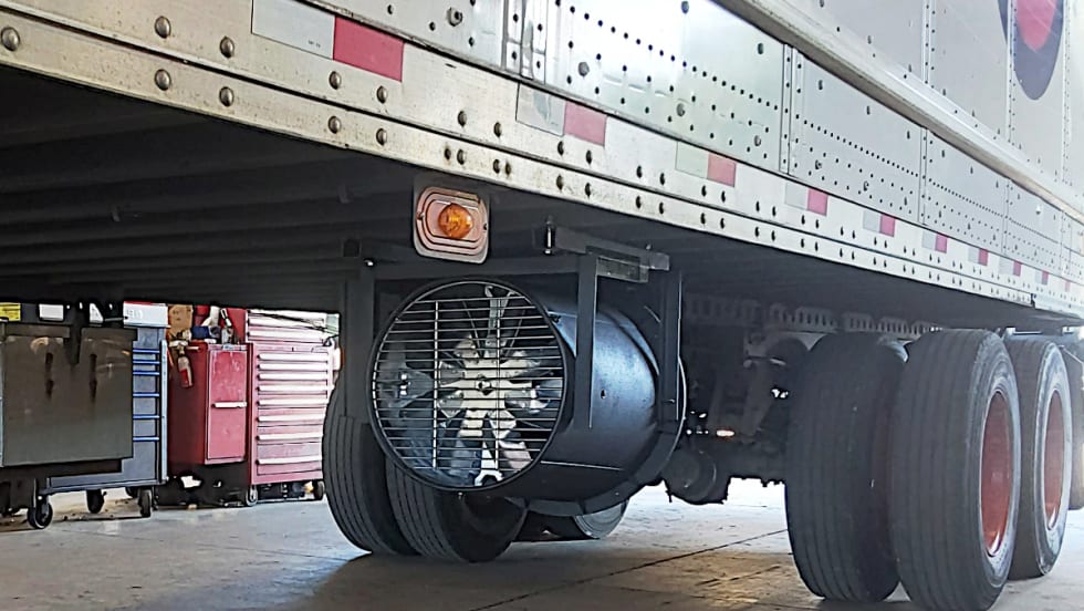 A cylindrical metal tube with fan blades is installed beneath a trailer.