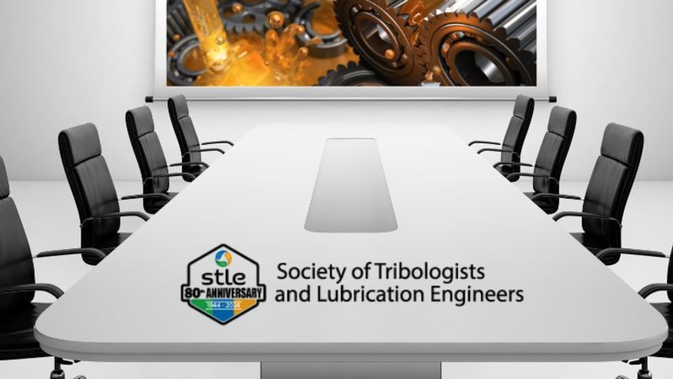 A stark white boardroom table, black chairs on either side, and a projection screen with an image of oil flowing over gears.