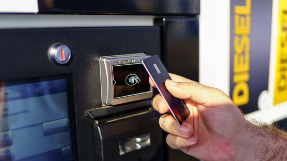 Close up of hand holding a fuel card at the payment portion of a fuel pump.
