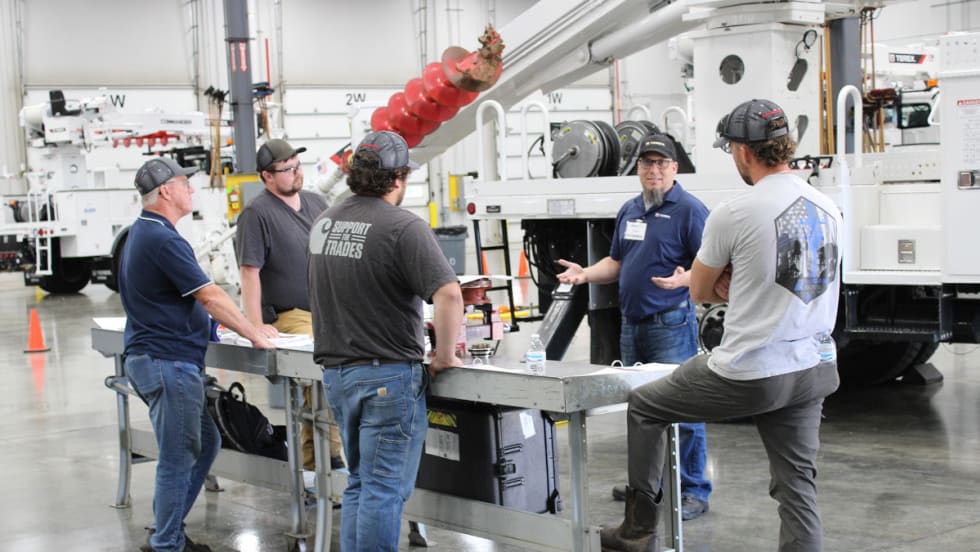 Men standing around a table in a warehouse, engaged in a discussion.