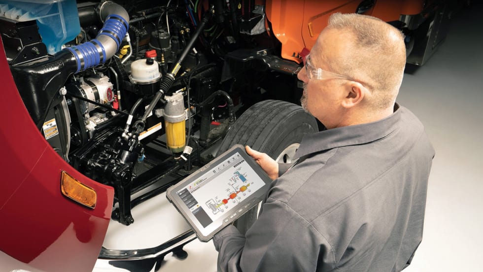 An man using a tablet to check the truck's engine.