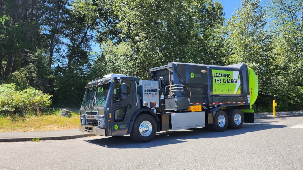A trash collection truck driving through a street with greenery.