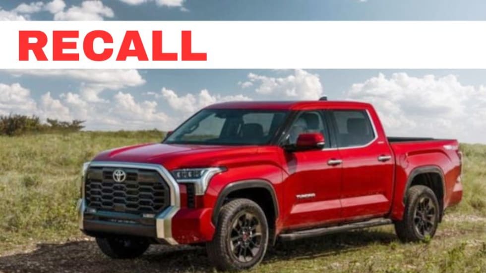 Red Toyota pickup truck in a grassy field, with the work RECALL in the upper left portion of image.