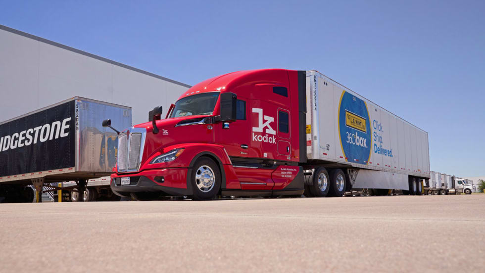 Red Kodiak Robotics truck tractor pulling J.B. Hunt 360 trailer with Bridgestone trailer in background.