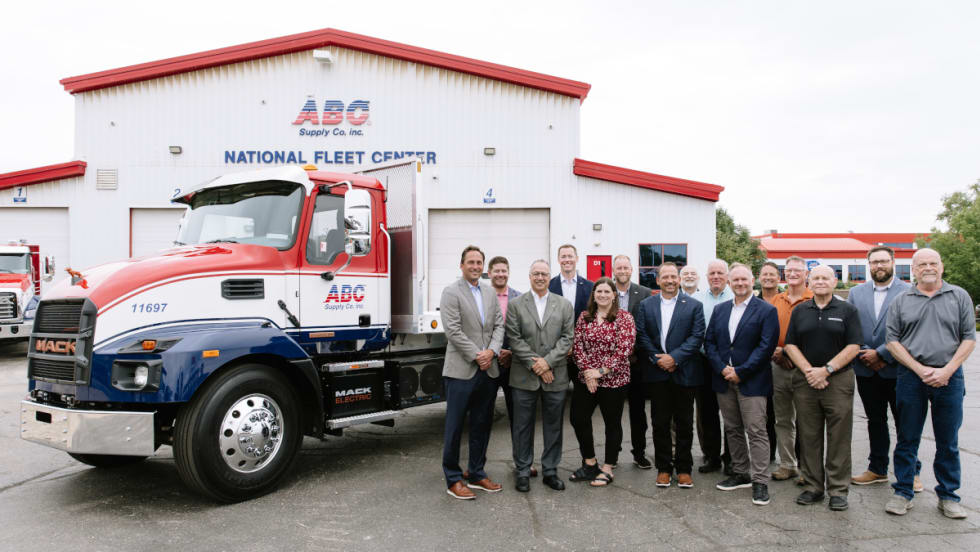 A group of people stands next to a medium-duty truck in front of a business, ABC Supply.