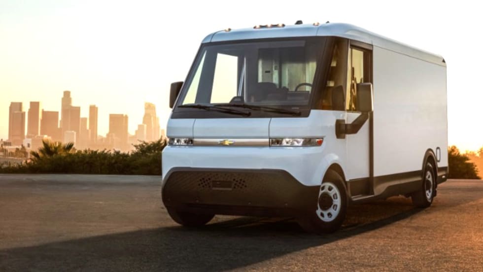 White EV delivery van in a parking lot with skyline behind it.