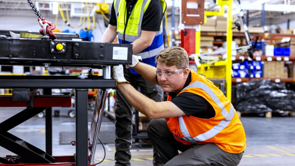 A man working diligently in a factory, surrounded by machinery and equipment, focused on his tasks.