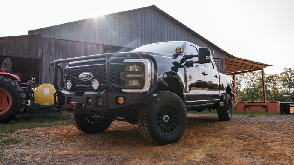 Angled view of a lifted black pickup truck parked in front of a barn.