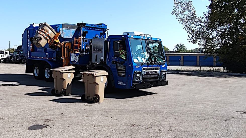 Refuse truck with side loader lifting a garbage can.