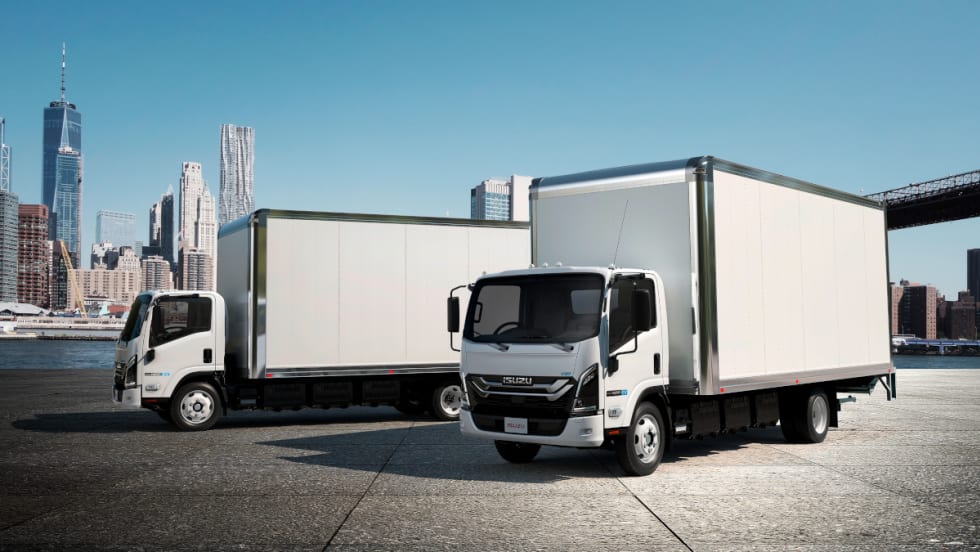 Two white box trucks parked in front of a city skyline.