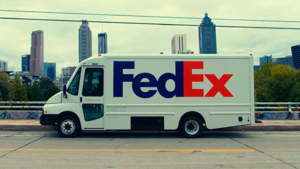 White battery-electric FedEx truck parked in front of a city skyline.