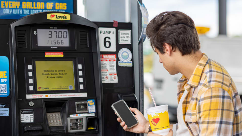 Young man looks at a fuel discount app while at a fuel pump.