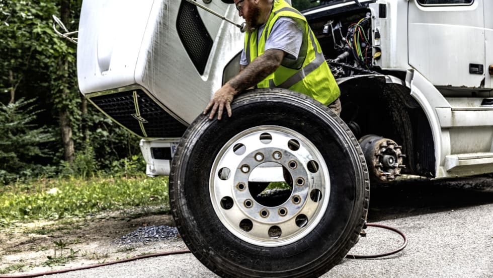 Man rolls a tire away during a roadside tire change.