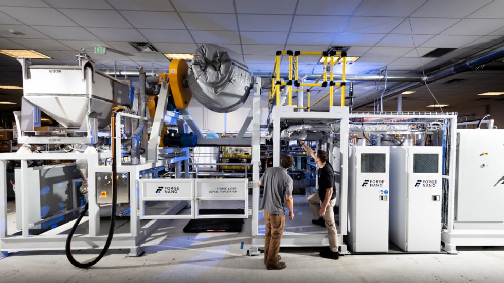 Two men stand in front of technical machinery.