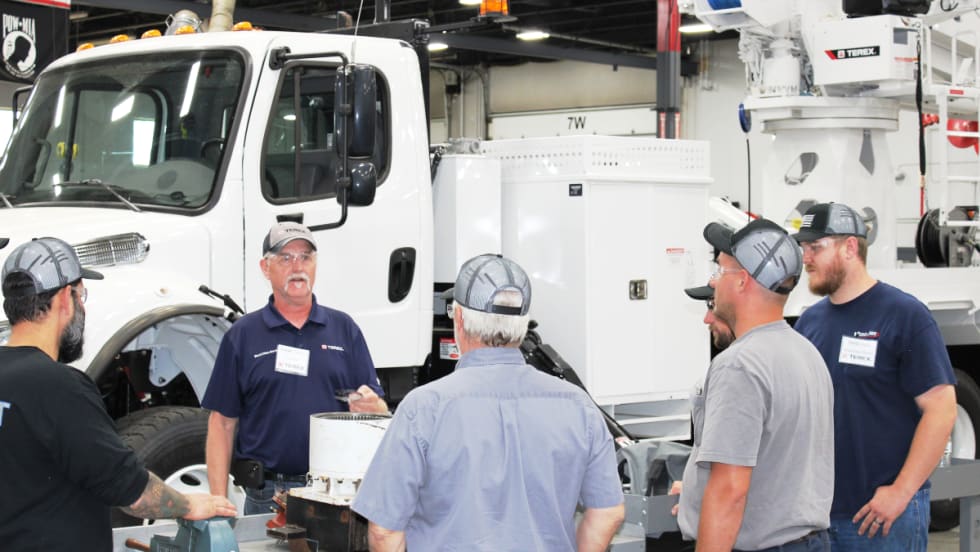 Group of men standing around a bucket truck being trained on maintenance.