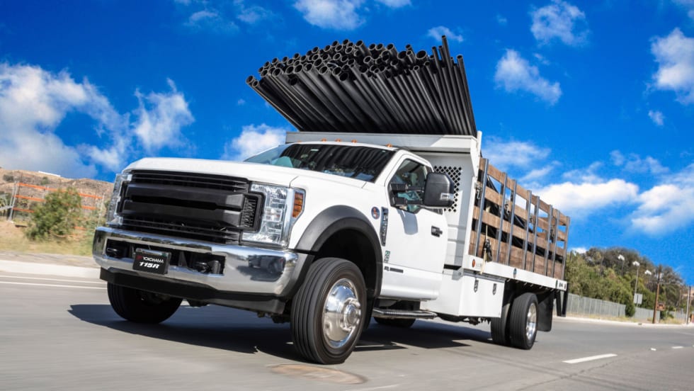 image of a white work truck hauling pipes extending over the cab
