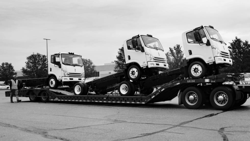Three chassis cab trucks are shown loaded on a trailer.