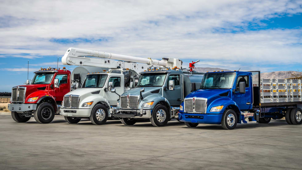 Photo of multiple medium-duty Kenworth trucks parked side by side.