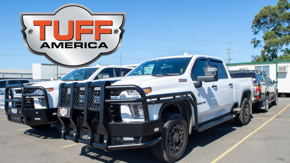 Two white pickup trucks with heavy-duty bumpers and side protection parked in a lot.