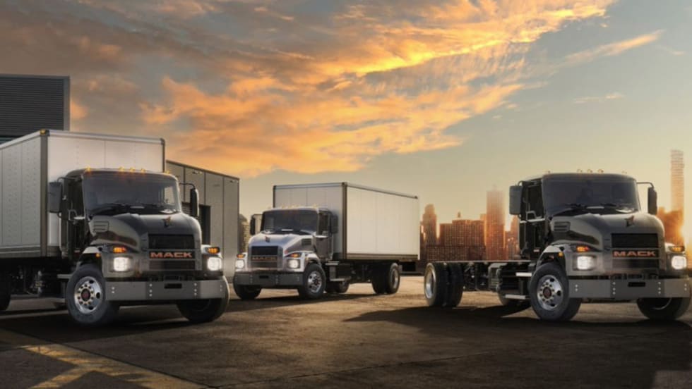 Three Mack electric trucks parked in front of a scenic afternoon sky.
