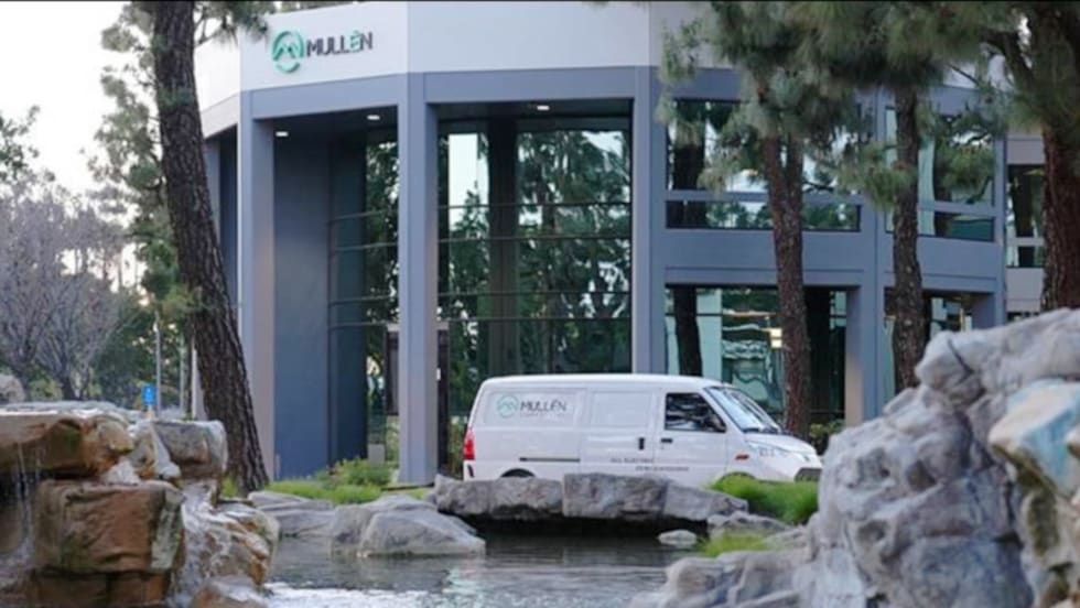White cargo van parked in front of a landscaped corporate building with Mullen logo.