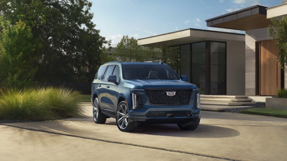 Sunny outdoor shot of a blue 2025 Cadillac Escalade SUV in the drive way of a house.