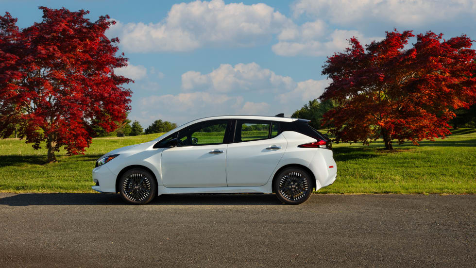 A white Nissan Leaf is shown parked by two trees.