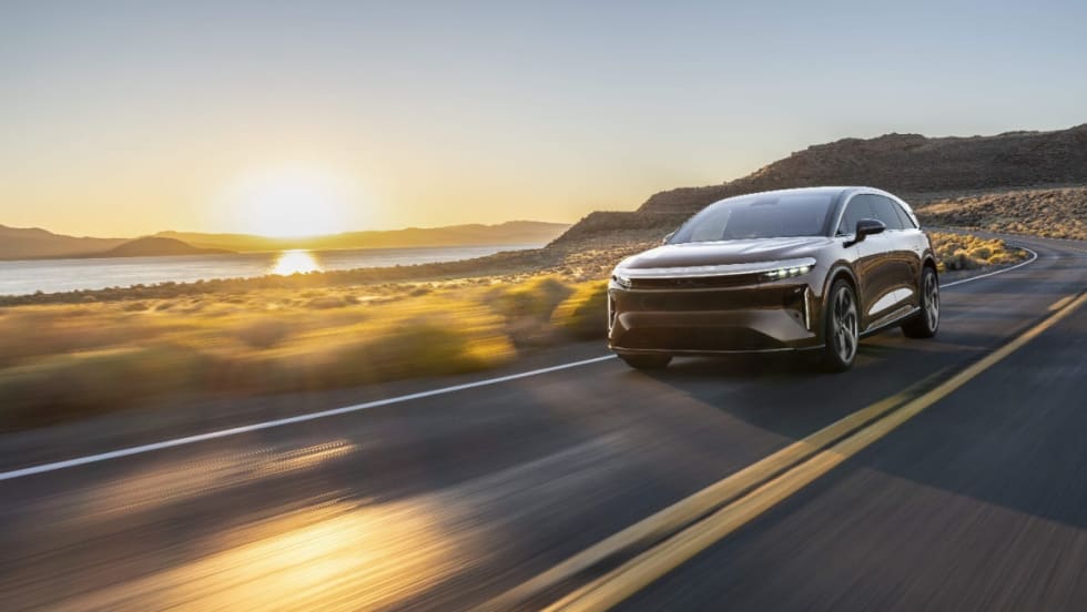 Lucid Gravity electric SUV driving on an open highway at sunset, showcasing the vehicle equipped with advanced navigation and positioning technology.