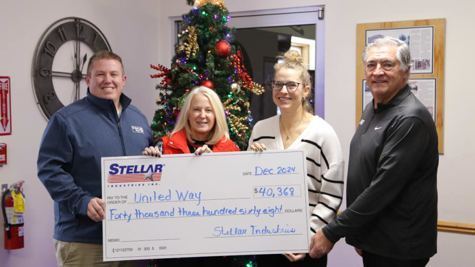 Four business people hold a large symbolic check as part of a charitable donation. 