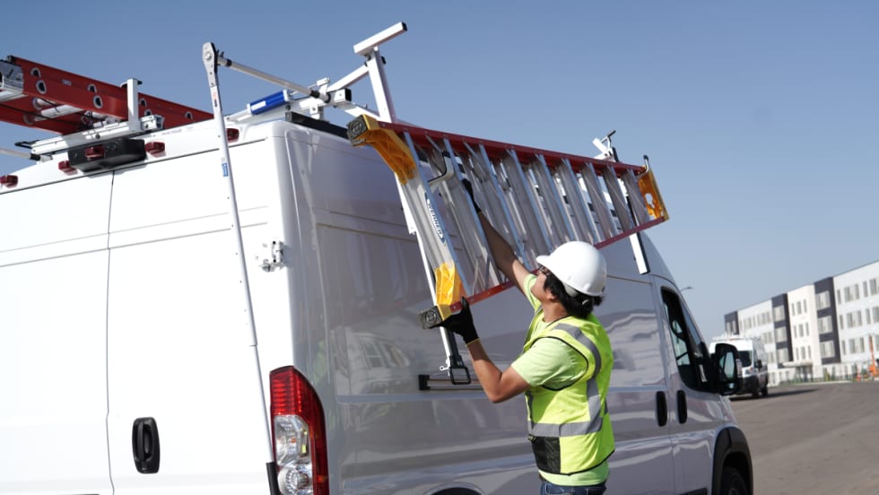 Man unloads ladder of the rack of a work van.